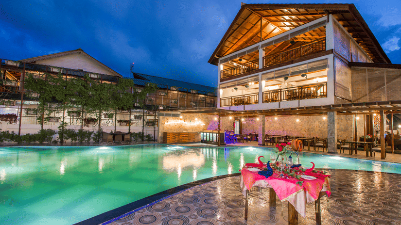 A table next to a swimming pool decorated with pink sheets and the facade of Symphony Summer Sand Beach Resort And Spa, one of the best resorts in the Andaman Islands, at the background.