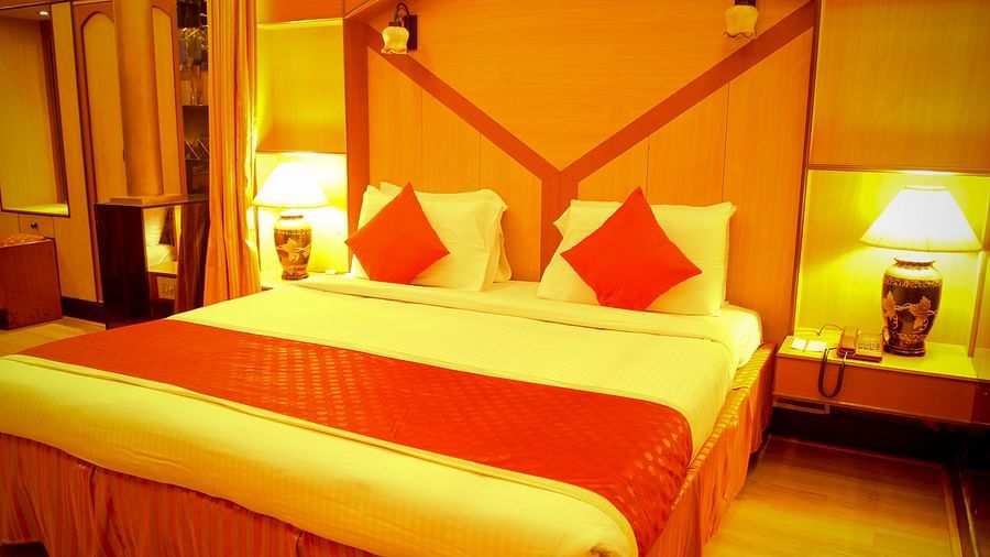 Hotel Yasodha Towers - Interior view of the bedroom featuring a king size bed with brown and yellow decor in yellow lighting 