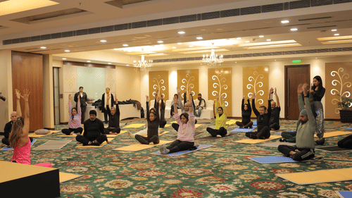 A group of people performing yoga by stretching their hands by sitting on a yoga mat at Heritage Village Resorts & Spa