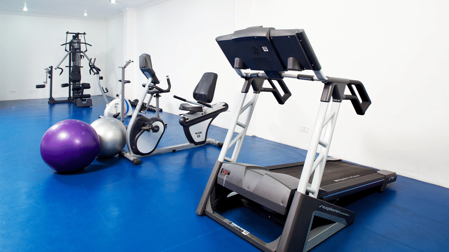 A gym room with a blue floor featuring a treadmill, an exercise bike, and fitness balls | Le Pondy