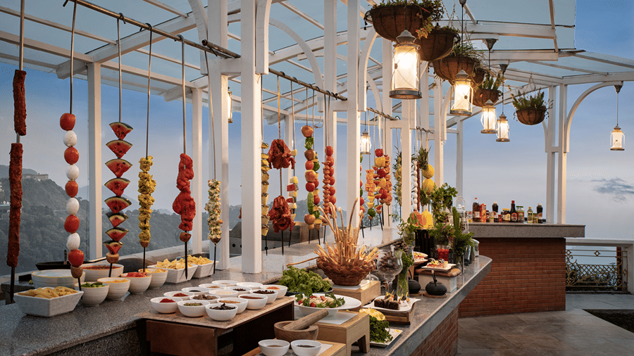 Food counters and colourful hanging decorations line a glass-roofed buffet area at Ramada by Wyndham Mussoorie Mall Road.