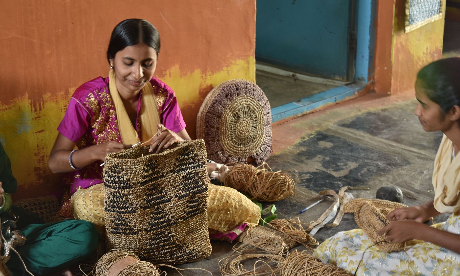 Two women crafting intricate items from natural fibers