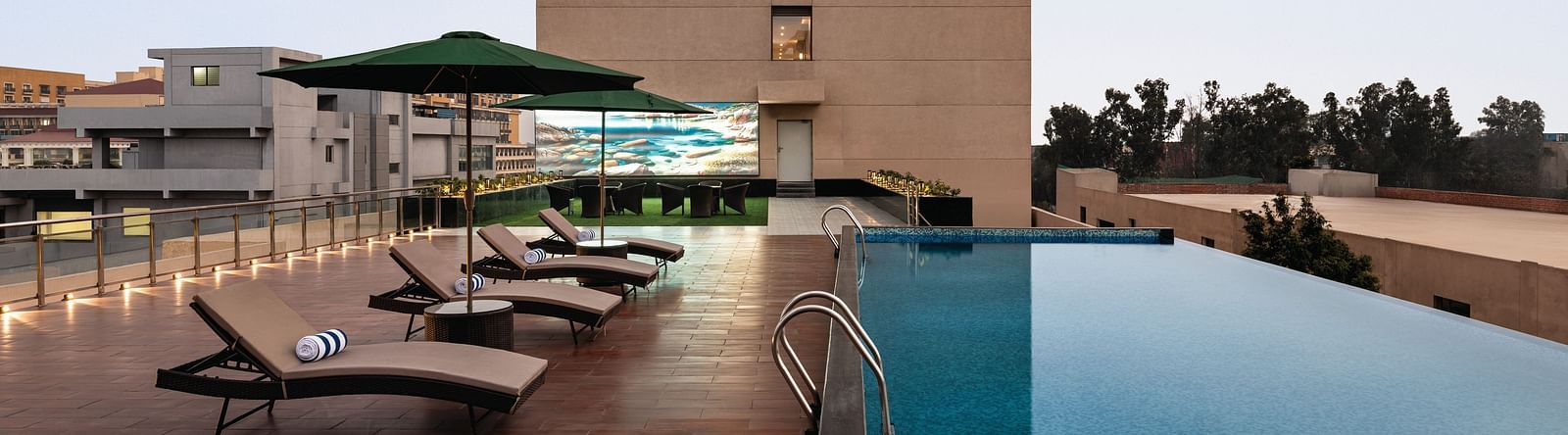 Ramada Encore by Wyndham, Bhiwadi | Hotel exterior with a pool, lounge chairs, and a clear blue sky.