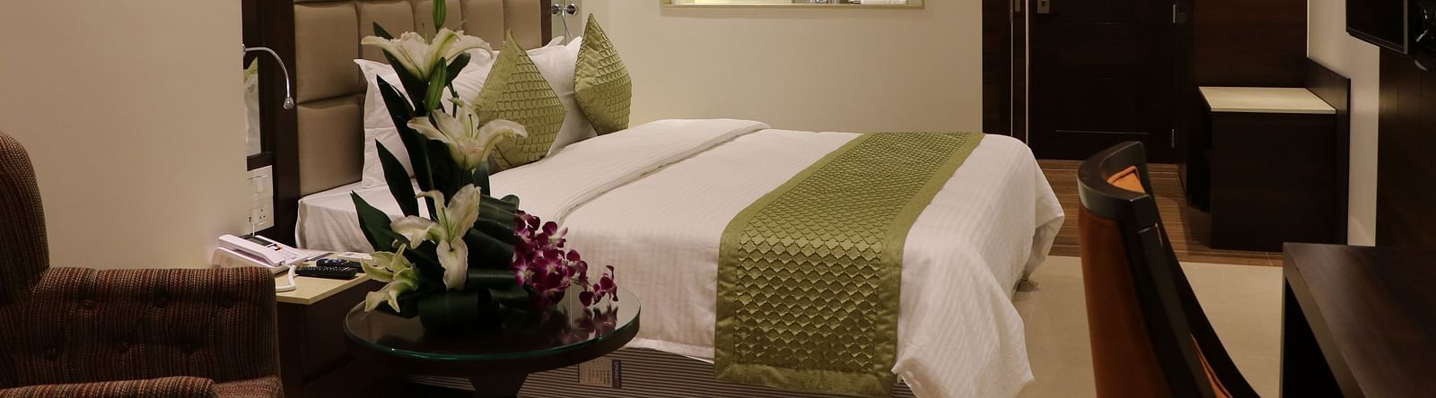 Side view of a room with a bed and a table with flowers beside it at Calux Grand Inn, Calangute.
