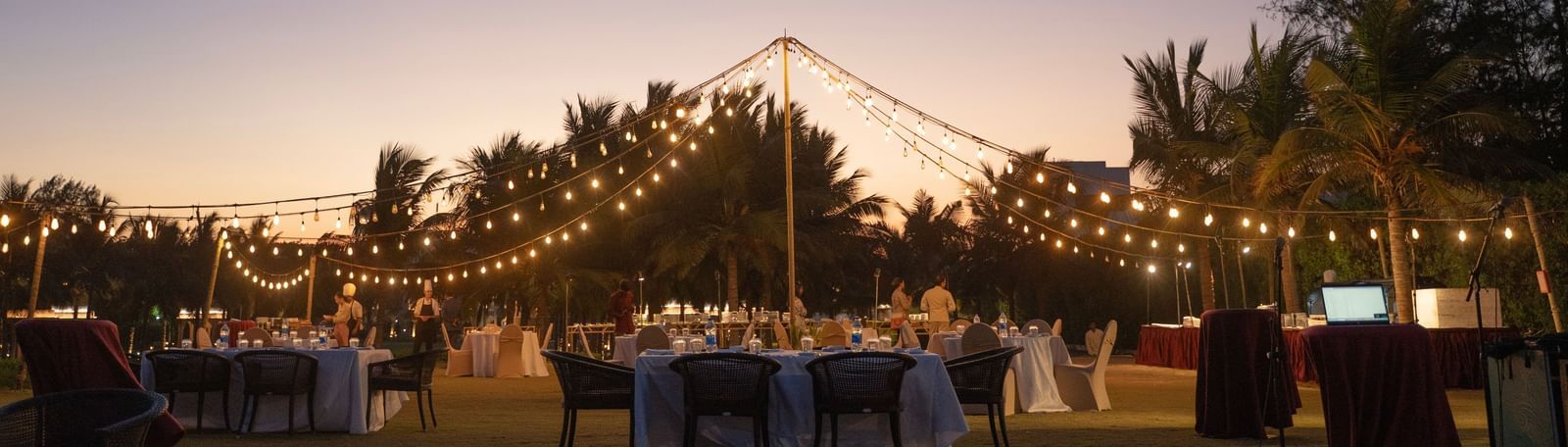 Outdoor evening event setup with string lights and a sunset backdrop - Kaldan Samudra Palace