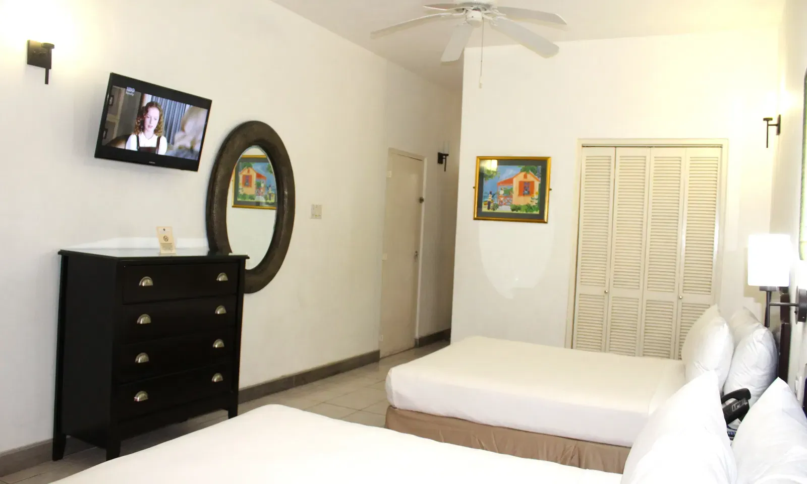A hotel room contains twin beds, a dresser with a mirror, and a television | Executive Double Room | Altamont Court, Jamaica