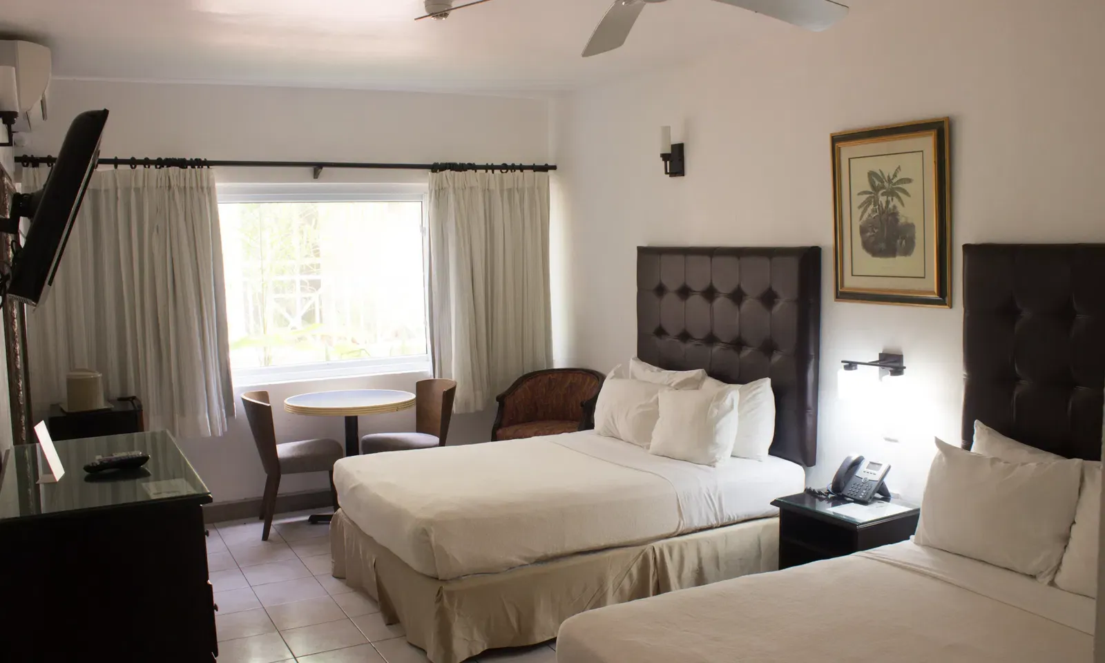 A spacious hotel room features two large beds, a sitting area with a table and chairs, and a window with curtains | Executive Double Room| Altamont Court, Jamaica