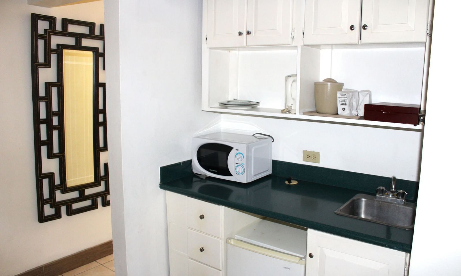 A kitchen area with white cabinets, a microwave, and a dark countertop | Junior Suite | Altamont Court, Jamaica