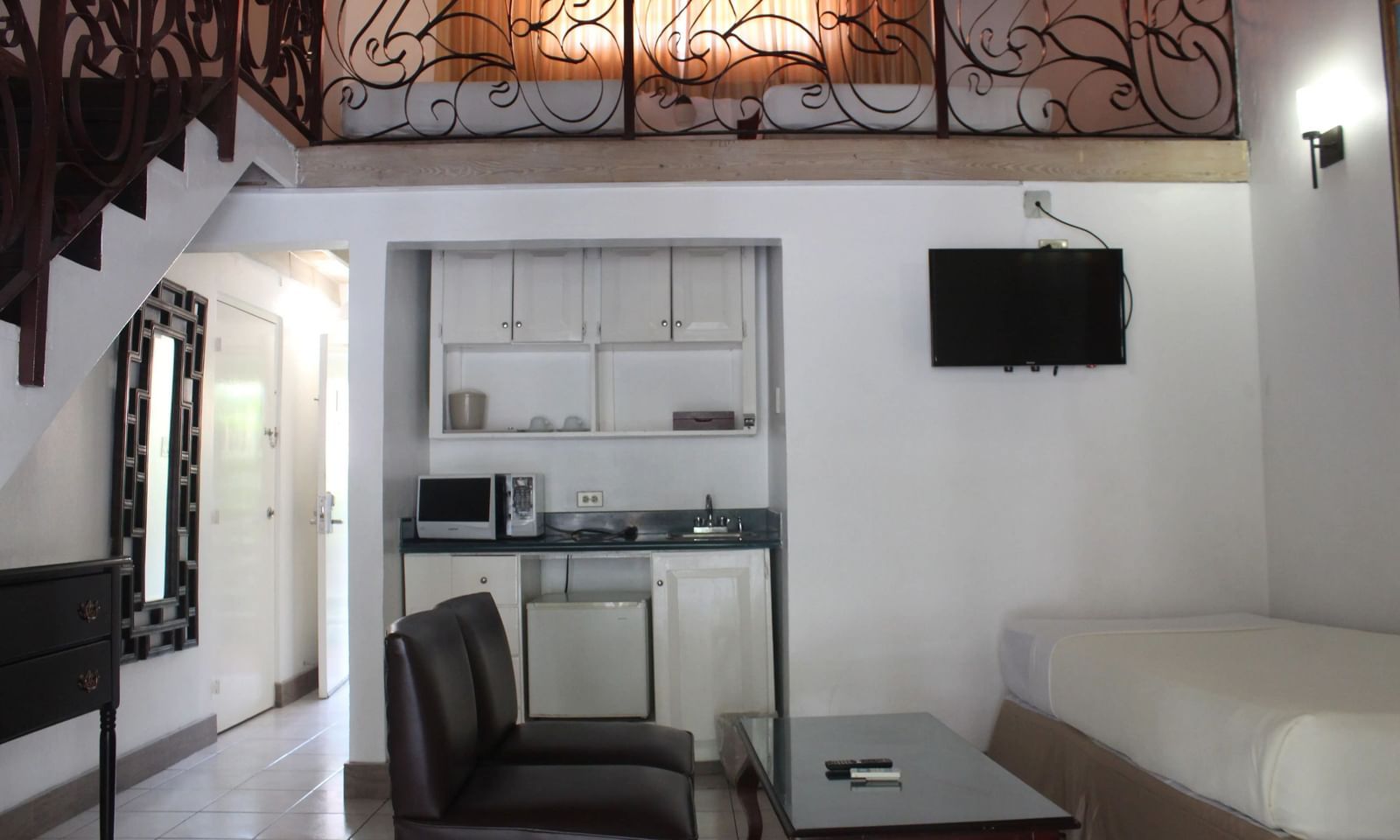 An interior shot of a room with a bed, a desk area, and a television, with a staircase leading to an upper level |Junior Suite | Altamont Court, Jamaica