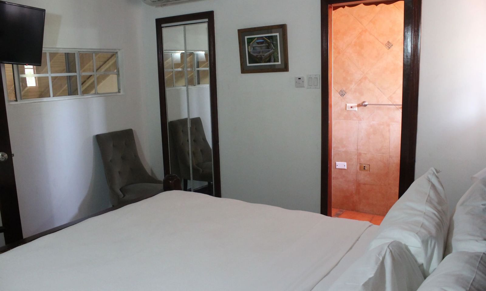 A brightly lit bedroom features a large bed with white linens and a glimpse of a doorway leading to another room | Superior Suite | Altamont Court, Jamaica