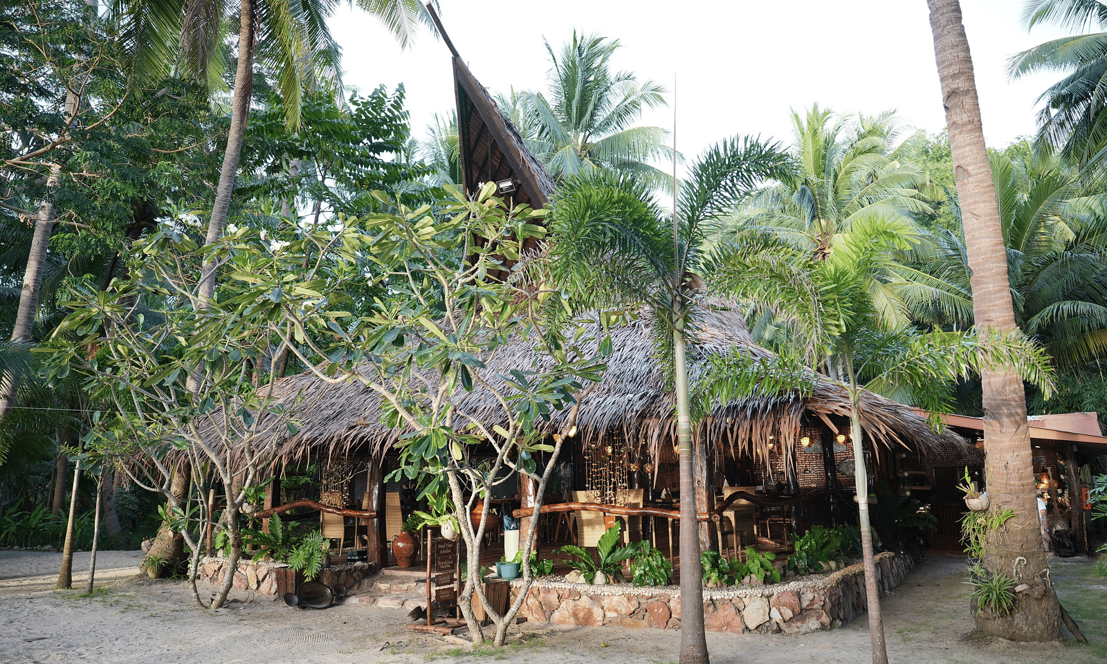 Garden hut with thatched roof and palm trees around at Flower Island Resort.