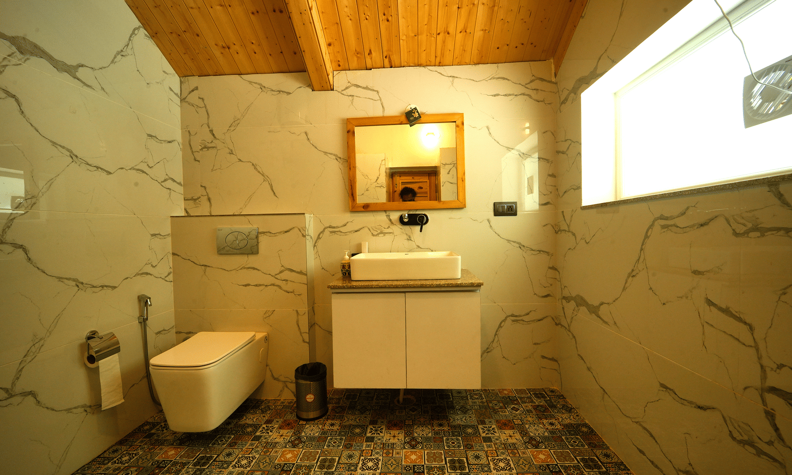 A contemporary bathroom with white marble-look tiles, a floating vanity, and wooden ceiling panels - Megha Resort & Villas, Dehradun