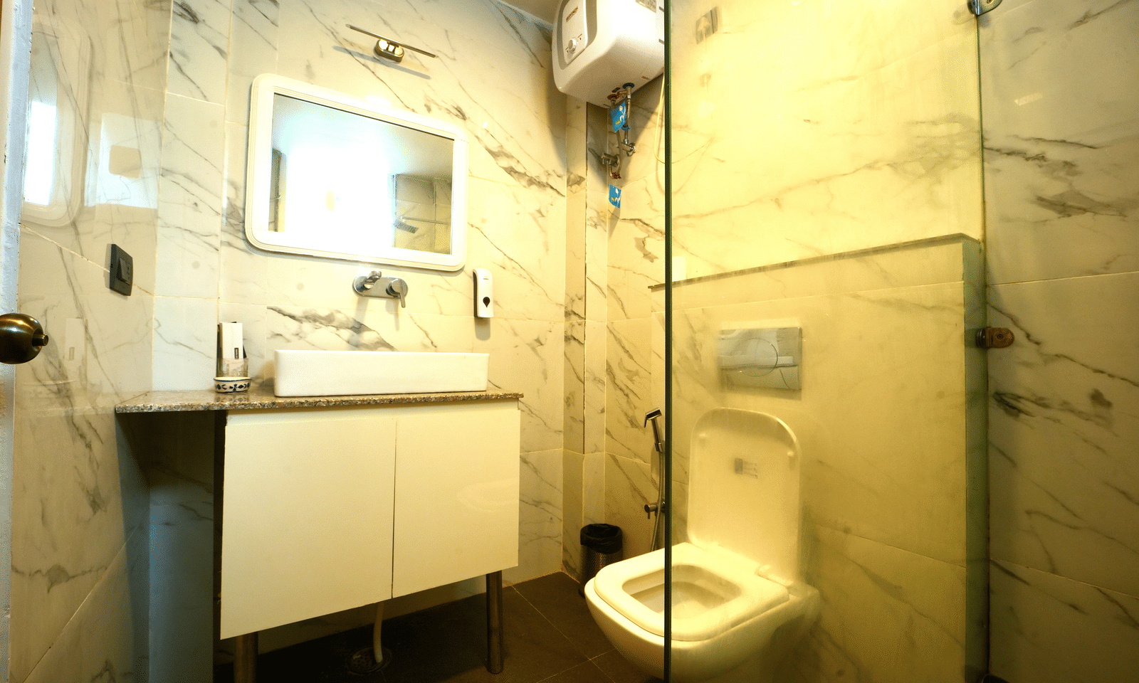 A clean, washroom with a white suite, mirror, and bright white marble-effect wall cladding - Megha Resort & Villas, Dehradun