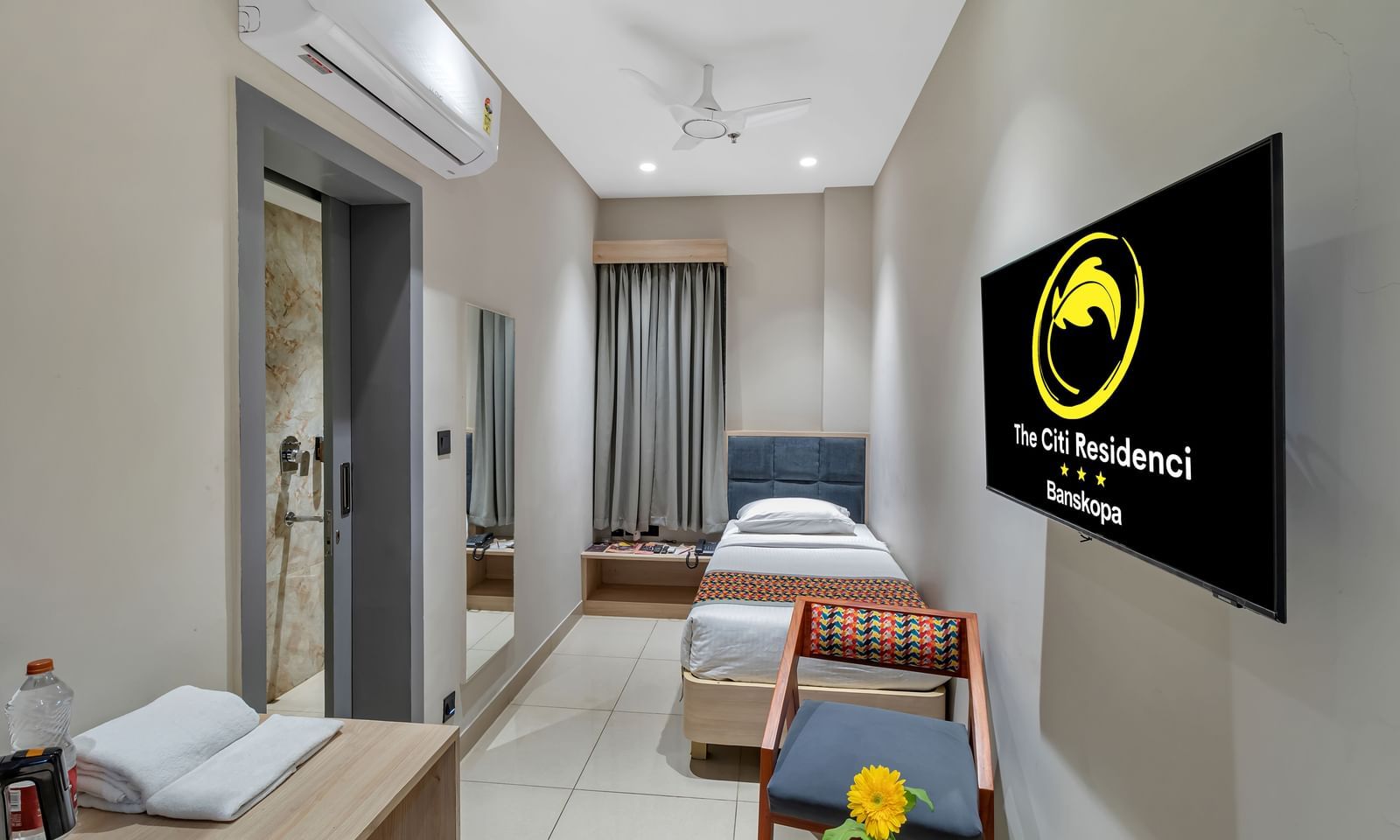 A compact hotel room with a single bed, a chair, a desk, and a wall-mounted television | The Citi Residenci Hotel Banskopa