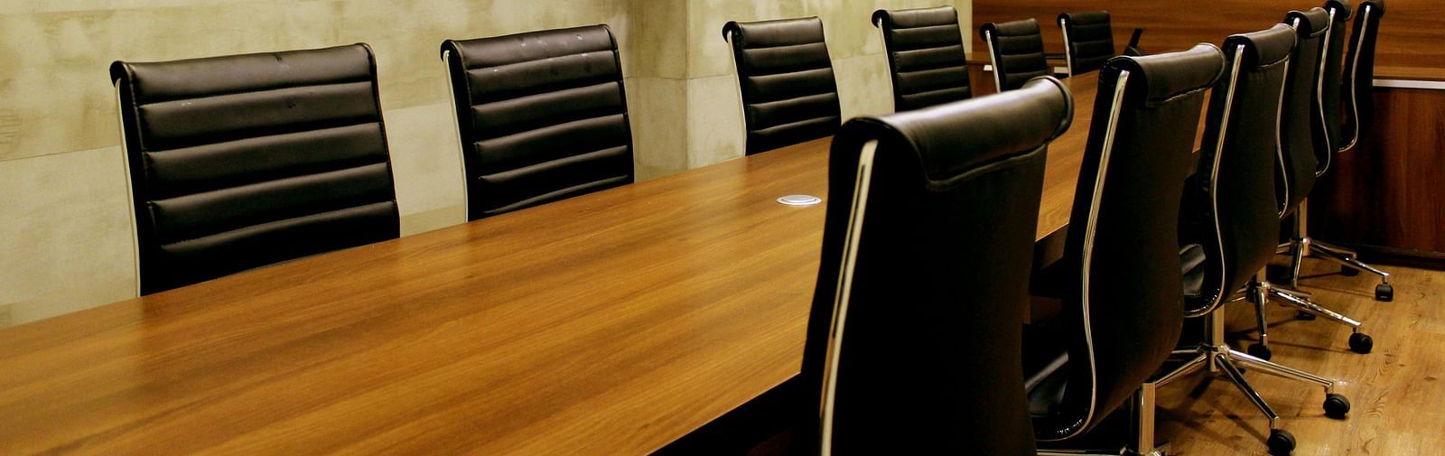 Modern conference room with a wooden table, black chairs, wall-mounted TV, and decorative shelves.