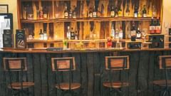 Bar counter with various alcohol bottles displayed and chairs placed in front of the counter