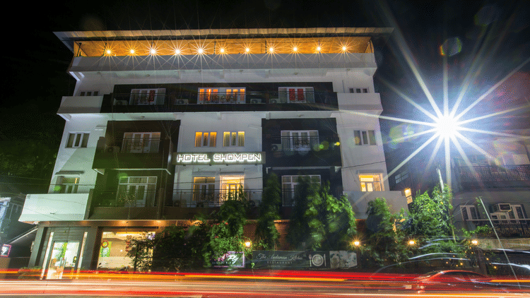 Hotel Shompen in Port Blair illuminated at night with bright lights and greenery at the entrance.