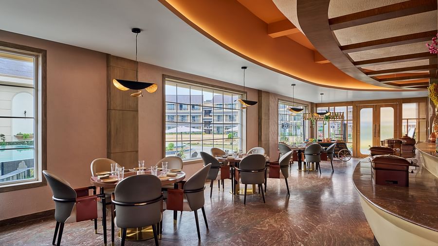 A brightly lit restaurant area features round dining tables with modern chairs set near large windows offering outdoor views. A curved counter runs along the right side of the space, which has a patterned floor and warm-toned walls - Voyage The Solitaire B