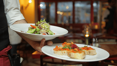 A person in a restaurant holding 2 plates with delicious cuisines in it that are well plated
