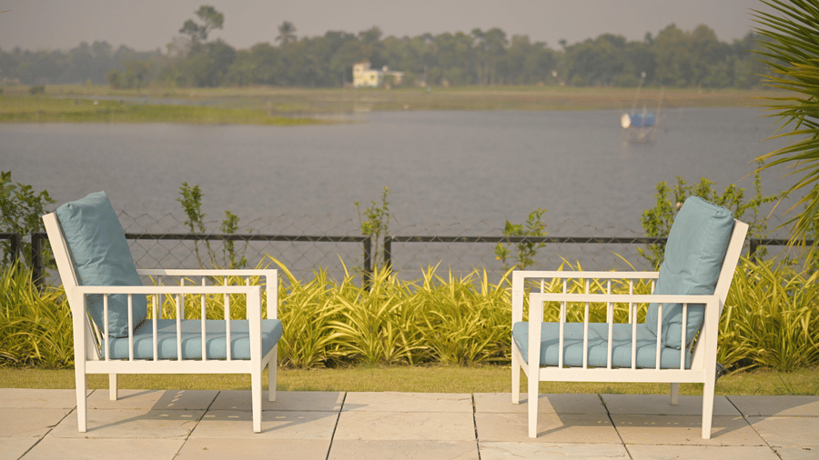 A riverside patio with 2 outdoor chairs facing the water, creating a calm retreat at Hotel Sonar Bangla, Mayapur.