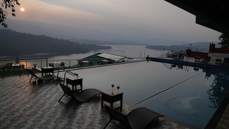 An image of the infinity waterfall swimming pool with lounge chairs placed beside it - Nisarga Lake Resort