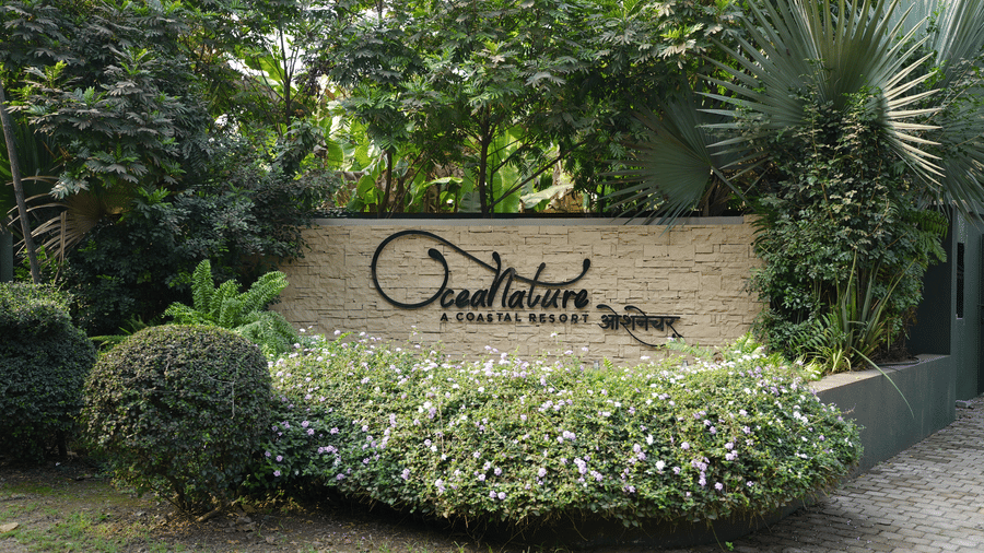 An outdoor stone sign surrounded by bushes and trees marks the entrance to Oceanature Resort, Alibaug.