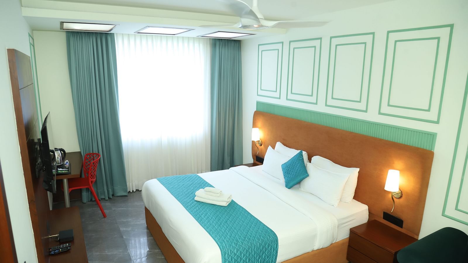 A comfortable room includes a double bed with a turquoise accent and wooden furniture - Asian Suites IFFCO Metro, Gurgaon