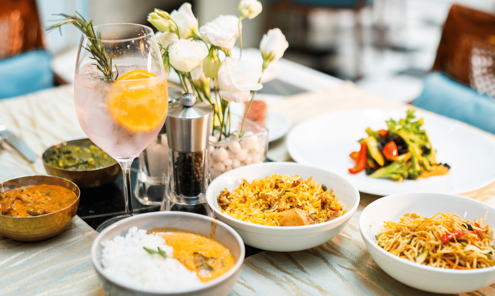 Elegant brunch spread with gourmet dishes, including biryani, curry with rice, stir-fried noodles, and grilled vegetables, served with a refreshing citrus cocktail