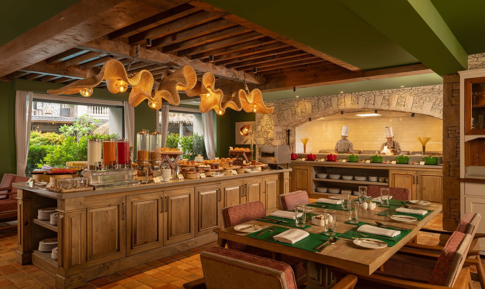 A wide-angle shot of Mila Restaurant at The Evren, Vagator, featuring a buffet counter in the middle of the dining area surrounded with well-arranged tables with cutlery and napkins.