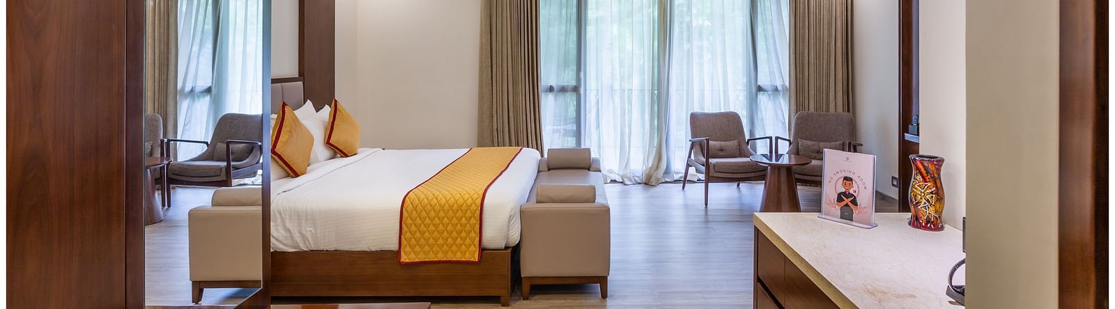 An image of a bed room with king size bed, a dressing tabel with mirror, a table at one corner  and two chairs at another corner - The Silver Sky