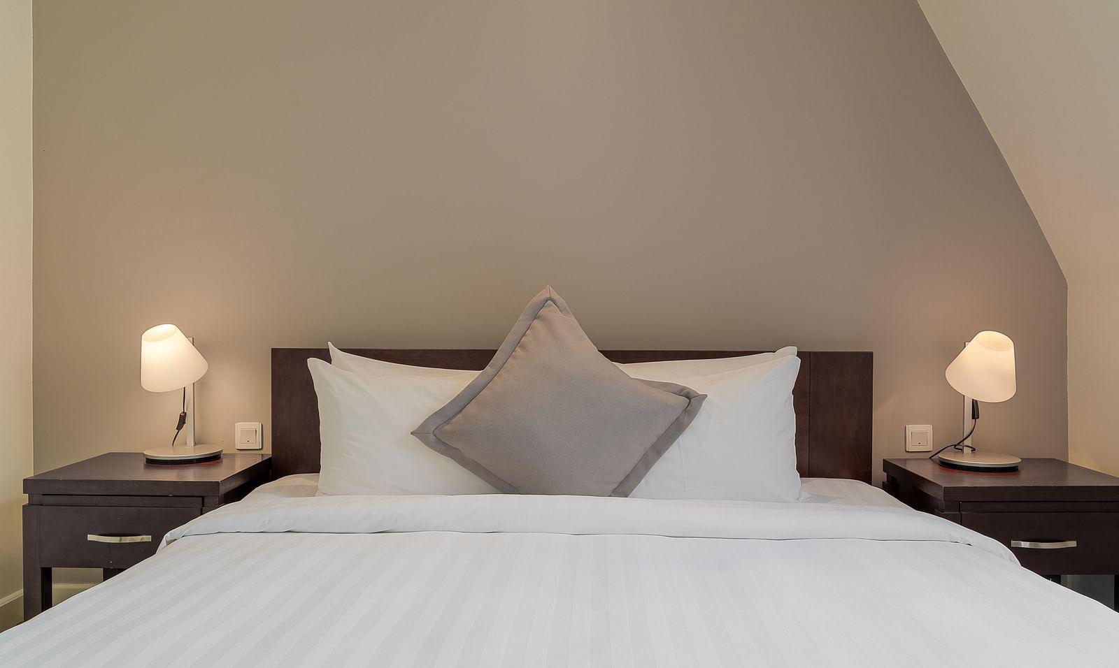 A cosy bedroom with a white bed, bedside tables, and lamps under a sloped ceiling | Four-bedroom Suite | Central Mansions, Phnom Penh