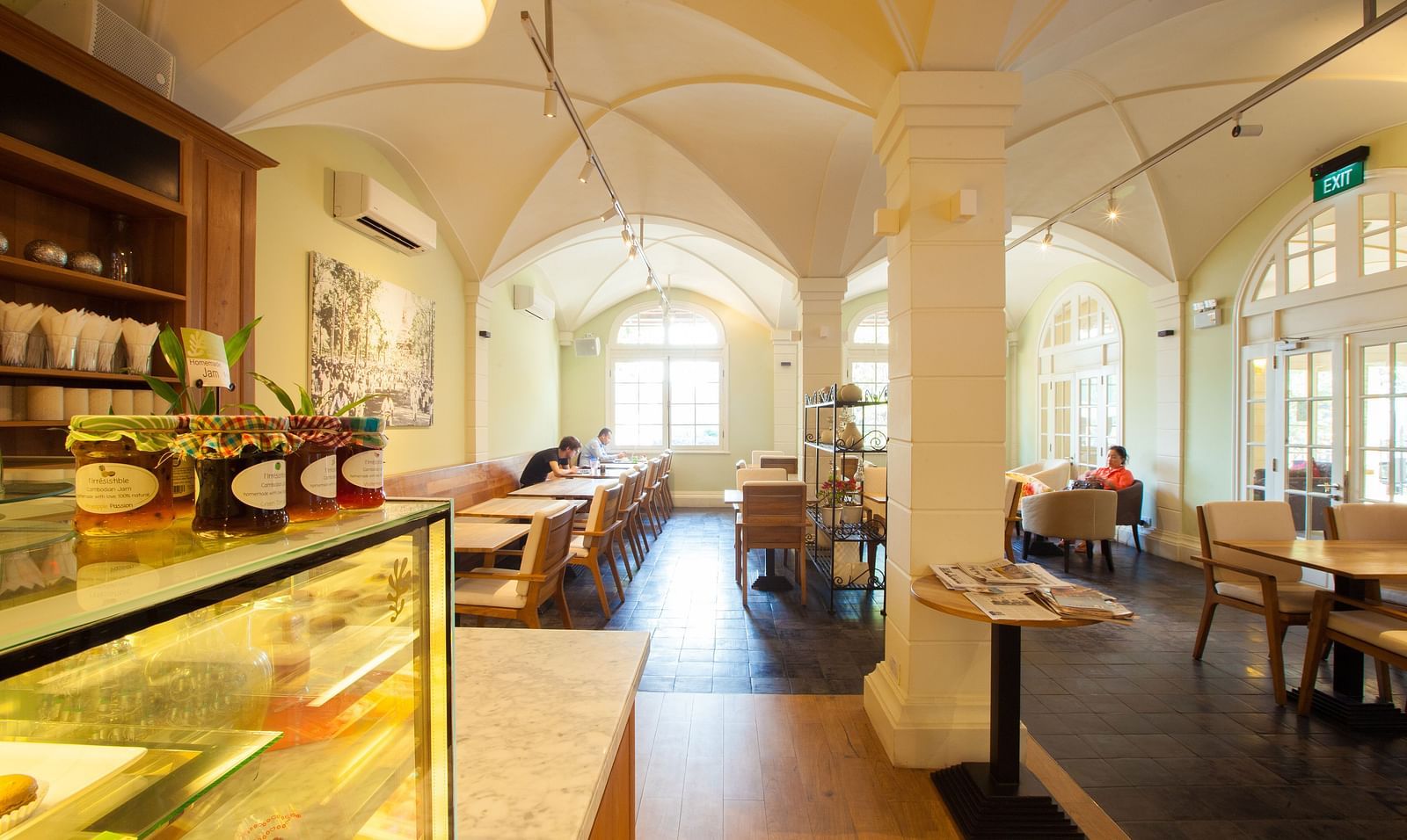 A cafe interior with tables and chairs, display shelves, and a long counter | The Shop | Central Mansions, Phnom Penh