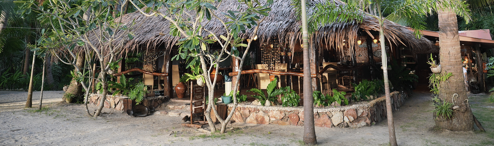 Garden hut with thatched roof and palm trees around at Flower Island Resort.