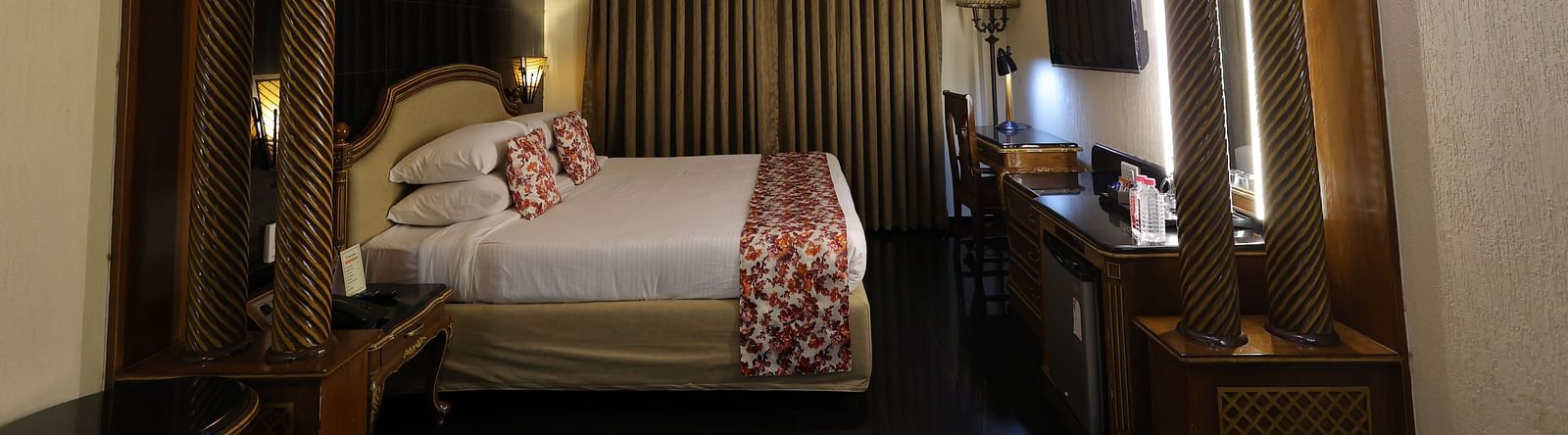 Close up  image of Premium room at Hotel Amar with a bed, table and long curtains.