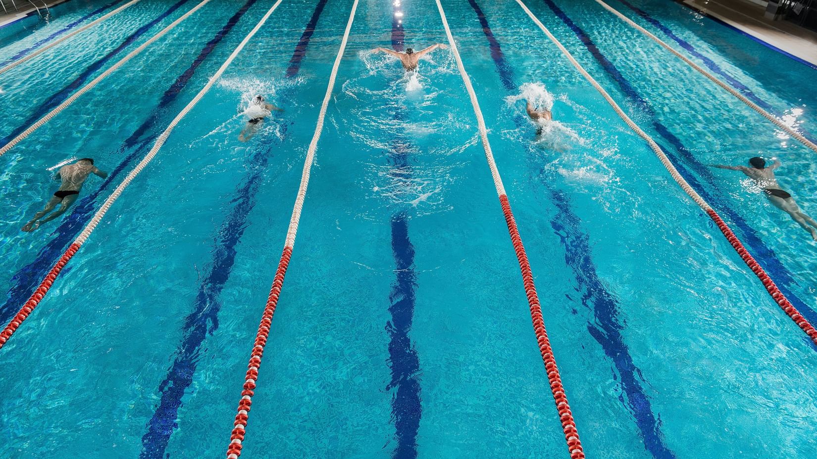 Asian Swimmers competing in a championship event in a six-lane outdoor swimming pool.