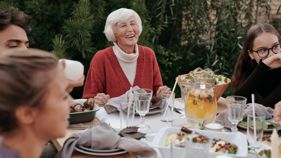 Family gathered around an outdoor dining table, sharing a joyful meal with drinks and laughter
