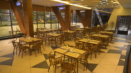 A wide view of a restaurant interior featuring wooden support beams and numerous dining sets at Hotel Sonar Bangla, Mayapur.