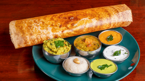 A Dosa platter served with traditional South Indian sides like sambar, coconut chutney, and tomato chutney.