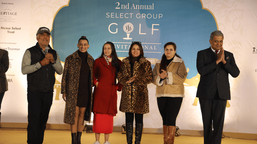 Six people standing on a stage with a man holding a mike with him.- Heritage Village Resorts & Spa