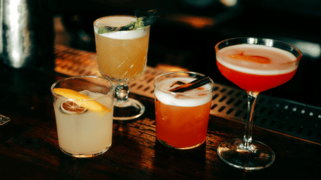A selection of colourful cocktails in different glassware, garnished and arranged on a dark wooden bar counter.