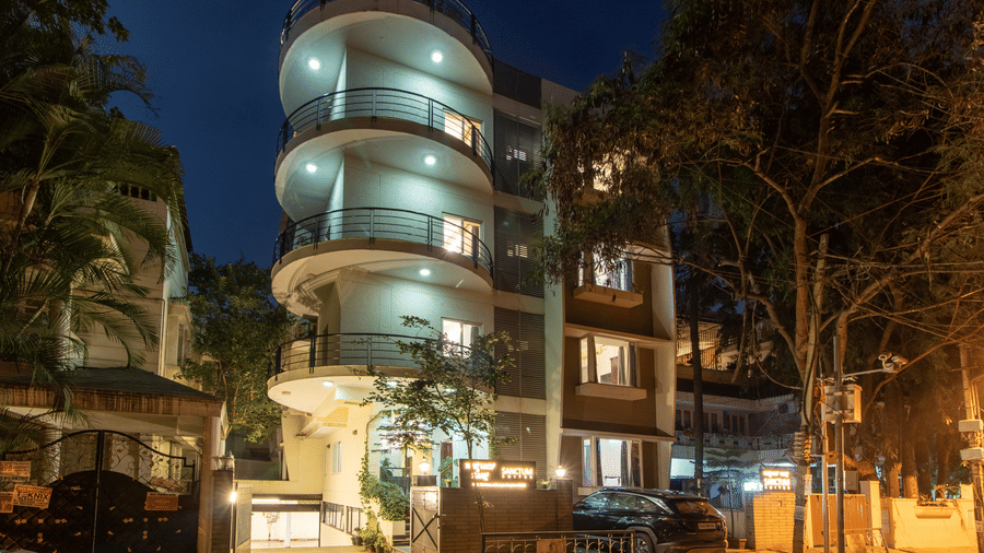 Night view of the hotel building with illuminated façade and curved architectural details at Sanctum Suites Indiranagar, Bangalore.