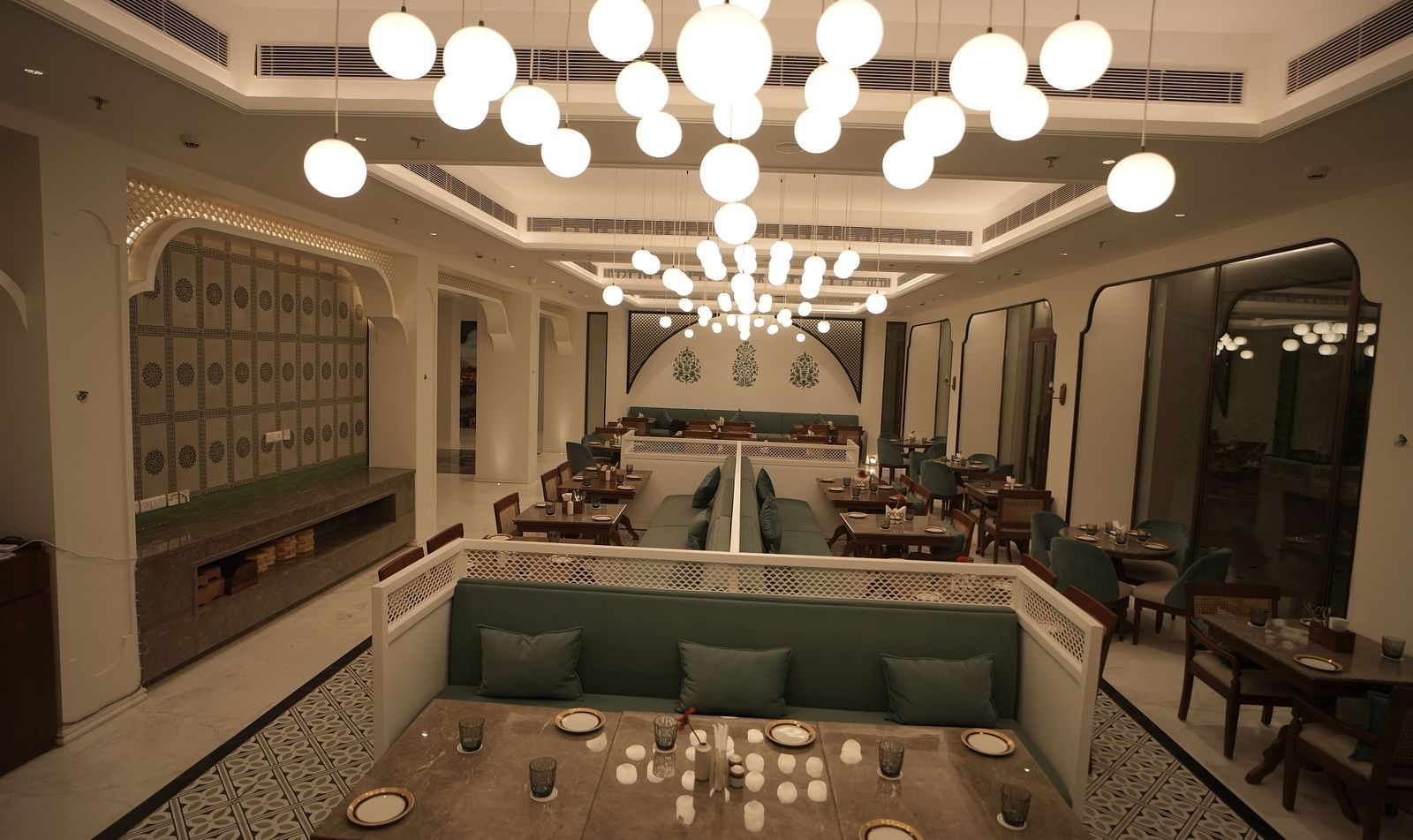 Full view shot of a restaurant with ample of warm lighting featuring well arranged dining tables along with cutlery Bhagirathi by RDB Atishay.