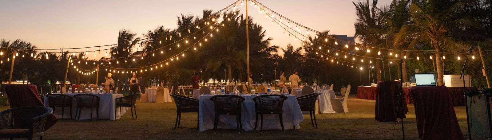 Outdoor evening event setup with string lights and a sunset backdrop - Kaldan Samudra Palace