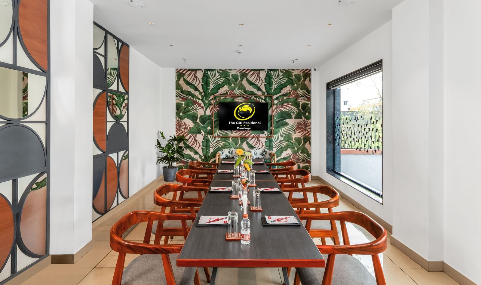 A modern meeting room with a long table, wooden chairs, a tropical-themed wallpaper, and a wall-mounted screen | The Citi Residenci Hotel Banskopa
