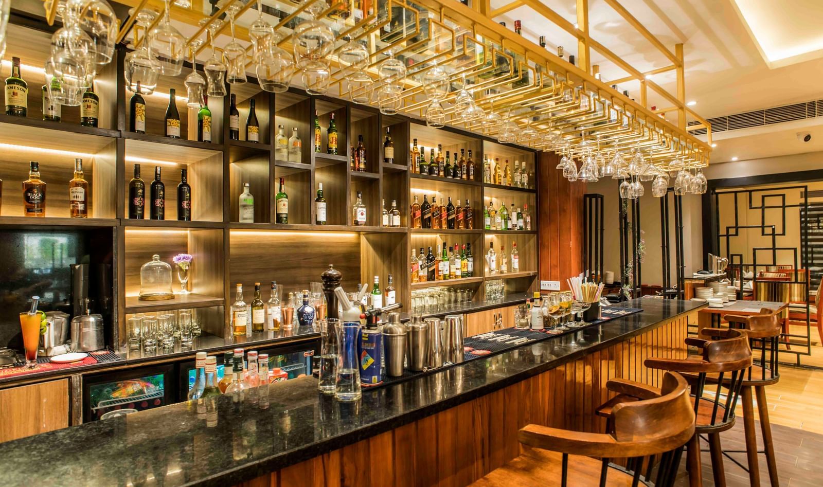 Well-stocked hotel bar with a dark countertop, multiple stools, and illuminated liquor bottles | The Citi Residenci Hotel Durgapur