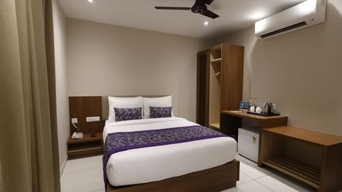 A deluxe room at Pride Biznotel Canopus Digha featuring a bed, bedside table on either side, air conditioner, fan, a cabinet table where tea and coffee maker is kept