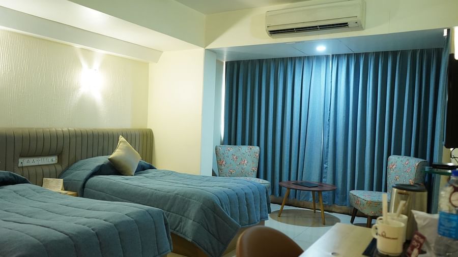 An image of a bedroom with twin beds, AC, table and chair, and two single sized sofa