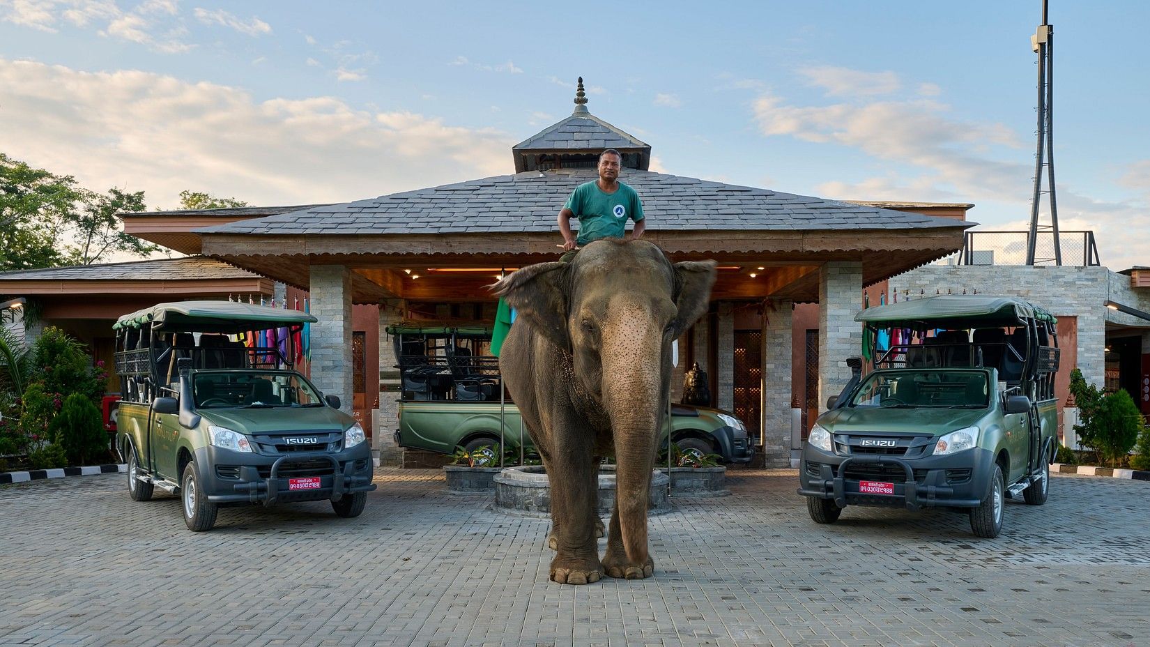 Hotel entrance with safari jeeps and an elephant, offering a unique experience - Royal Tulip, Chitwan