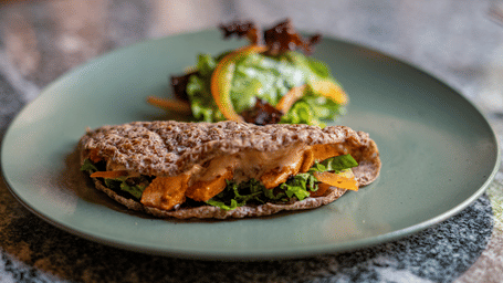 A vegetable and meat wrap served with a green salad on a teal coloured ceramic plate.