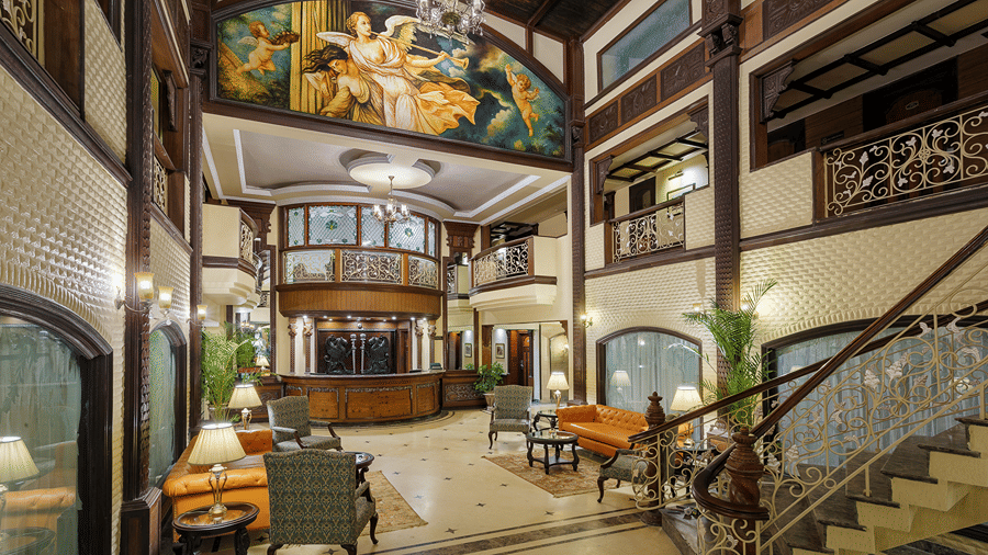 A multi-story lobby area featuring wooden banisters, seating areas, and a grand staircase at Ramada by Wyndham Mussoorie Mall Road.